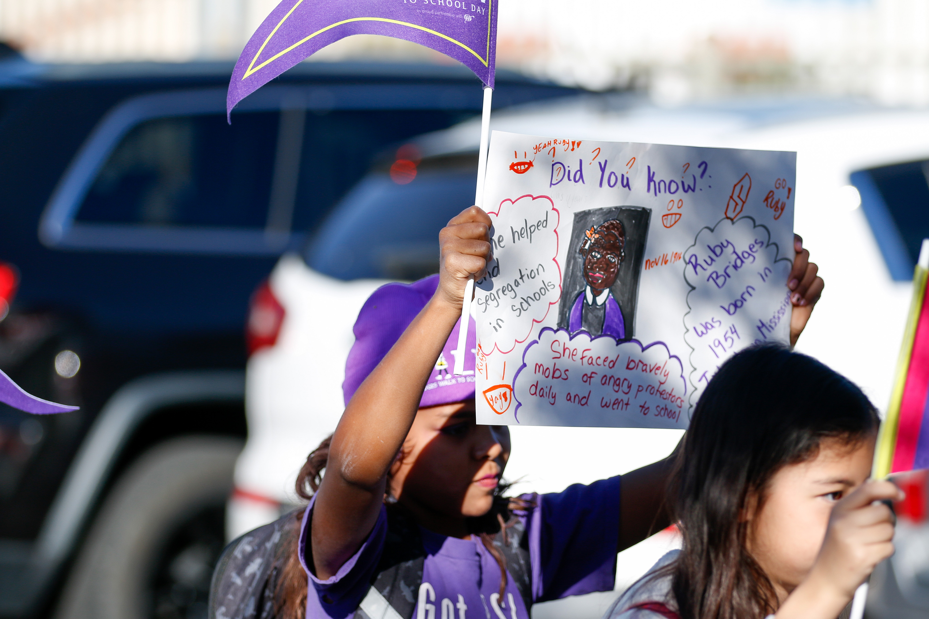 A girl in a purple beanie holds up a poster about Ruby Bridges