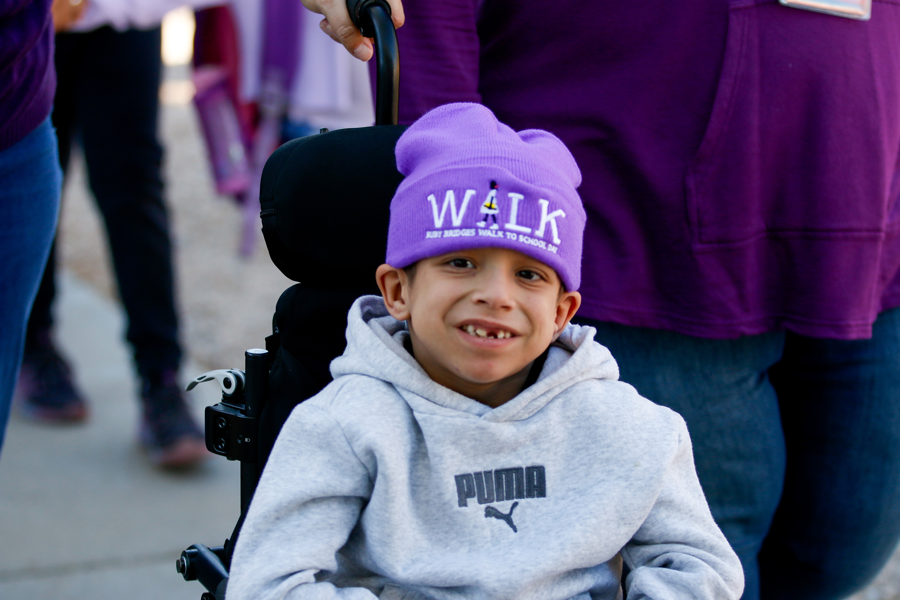 A little boy in a gray sweatshirt and purple beanie smiles during the walk