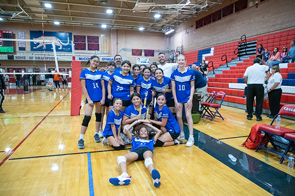 Miles' girls volleyball team poses with their trophy on the court