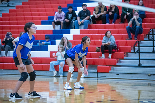 Two girls crouch on the court waiting for the volleyball to come over the net