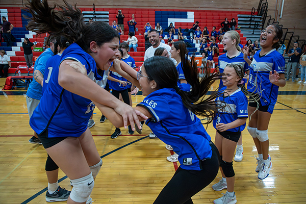 The girls volleyball team jumps up and down cheering their win
