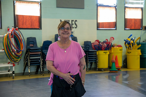 A woman in a pink shirt smiles in the school gym