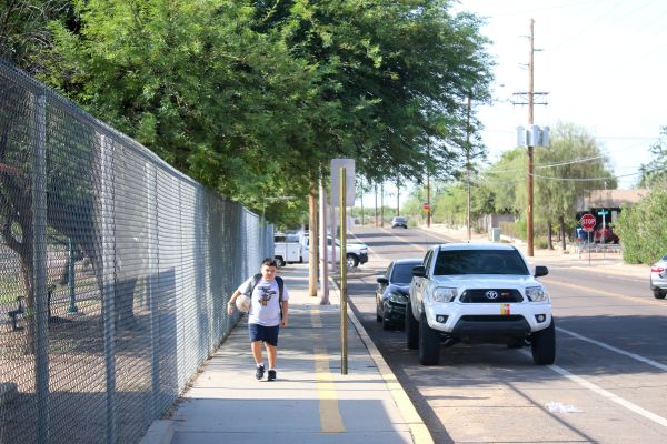 A boy holds a basketball under his arm as he walks to school