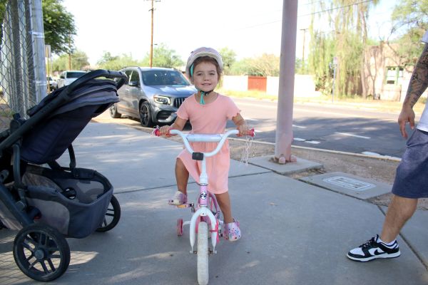 A little girl in a pink dress rides her bike to school